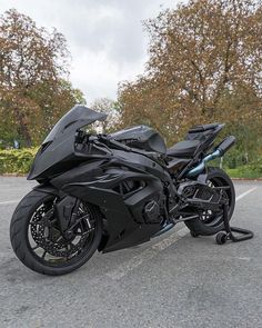 a black motorcycle parked in a parking lot next to some trees and bushes on a cloudy day