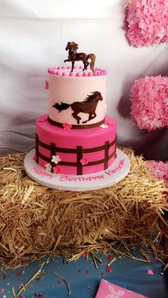 a three tiered cake with horses on top and pink frosting, sitting on hay bales