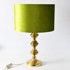 a gold lamp with a green shade on the base and a white cord plugged in