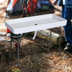 a white sink sitting on top of a field next to a camping table and tent