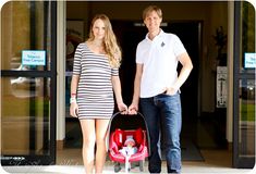 a man and woman holding hands while standing next to a baby in a stroller