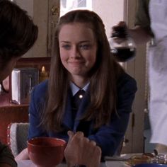 a woman sitting at a table with a cup in front of her and another person standing behind her