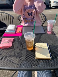 a person sitting at a table with a drink and notebooks on it, talking on the phone