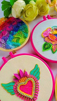 four embroidered hoop art pieces with flowers and hearts on them, sitting next to each other