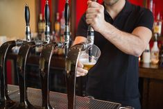 a man pours a beer from a tap at a bar with several taps behind him