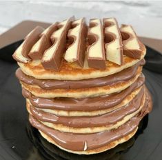 a stack of chocolate covered pancakes on a black plate with white and brown icing