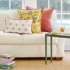 a white couch with colorful pillows on top of it next to a table and window