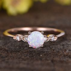 a white opal and diamond ring sitting on top of a rock