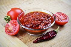 tomatoes and chili sauce in a glass bowl on a cutting board next to some peppers