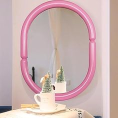 a pink round mirror sitting on top of a table next to a white coffee cup