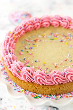 a cake with pink frosting and sprinkles on a white platter