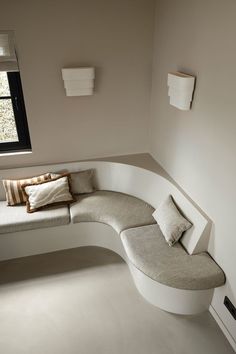 a corner bench with pillows on it in a room that has white walls and floors