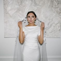 a woman in a white dress is holding her veil over her head and looking at the camera