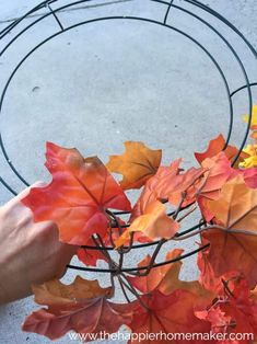 someone is holding leaves in front of a wire wreath with autumn colors on the outside