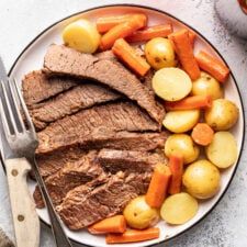 a white plate topped with meat, potatoes and carrots next to a knife and fork