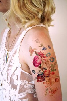 a woman's arm with flowers and butterflies tattooed on the back of her shoulder