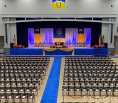 an empty auditorium with rows of chairs and blue carpeted area for the front of the room