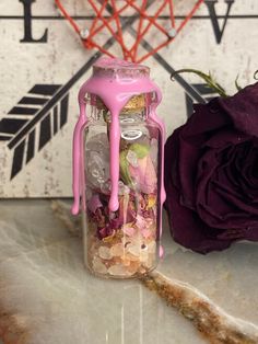 a jar filled with lots of different things next to a purple rose