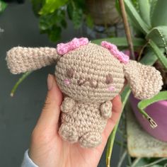 a small crocheted stuffed animal is held in front of a potted plant