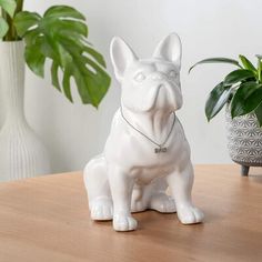 a white dog figurine sitting on top of a wooden table next to a potted plant