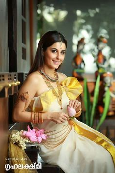 a woman in a yellow and white dress with jewelry on her neck posing for the camera