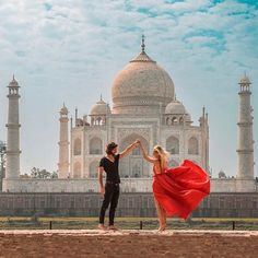 a man and woman standing in front of a white building with a red dress on