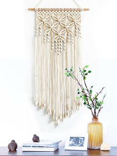 there is a vase with flowers on the table next to a macrame wall hanging