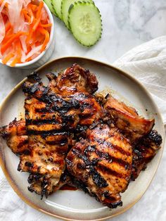 grilled chicken on a plate with sliced cucumber and carrots next to it