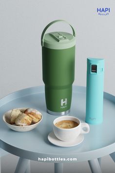 a cup of coffee and some food on a blue table with a green insulated thermos