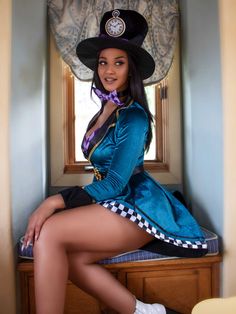 a woman in a blue dress and black hat sitting on a bench with her legs crossed