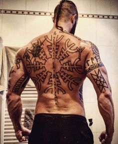 a man with tattoos on his back standing in front of a mirror