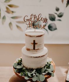 a white cake with a cross on top and greenery around the edges that says godbles always