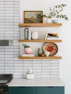 two wooden shelves on the wall above a stove and counter top with books, magazines, vases and other items