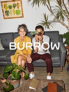 a man and woman sitting on a couch in front of a potted palm tree