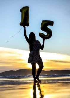 a woman is holding up the number fifteen and flying her kite on the beach at sunset