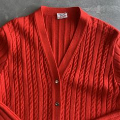 "Red cardigan long length with front pockets Construction: Stitched overlock at seams, front patch pockets, v neck with buttons, over the hip length Fabric: Orlon Acrylic knit / Lightweight but warm, washable, decreased wrinkles Tags: St Micheal Orlon / size 16 to fit 38\" bust / Made in Britain Condition: very good except missing buttons. missing 3 but extra one on side seam so missing 2, some minor pilling Size: Medium 38\" Bust c1970s, 1960s Measures: Shoulders: 17.5\" Bust: 38\" Waist: 34\" Red V-neck Outerwear With Button Closure, Classic Red V-neck Sweater For Fall, Red V-neck Cardigan For Work, Vintage V-neck Cardigan For Layering, Red V-neck Sweater With Button Closure, Red Long Sleeve Cable Knit Cardigan, Red Cable Knit Long Sleeve Cardigan, Red Knit V-neck Cardigan, Red V-neck Knit Cardigan