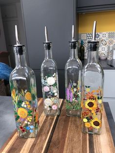 three glass bottles with flowers painted on them sitting on a wooden table in a kitchen