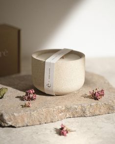 small pink flowers sitting on top of a stone slab next to a box with a white ribbon