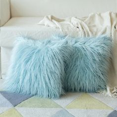 two fluffy blue pillows sitting on top of a white couch next to a pillow case