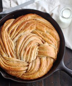 a skillet filled with bread on top of a wooden table next to a glass of milk