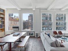 a living room filled with furniture and large windows next to a book shelf on top of a hard wood floor