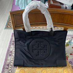 Brand New Never Used Tory Burch Ella Tote In Black Has Two Inside Pockets Large Tote To Hold A Lot Magnetic Closure And Two Buttons On Each Side To Close Up Too 17 L X 12.5 H X 7.5 W Tory Burch Ella Tote, Ella Tote, Tory Burch Ella, Tory Burch Tote, Zip Tote, Mini Tote Bag, Tory Burch Bags, Nylon Tote, Tory Burch Bag