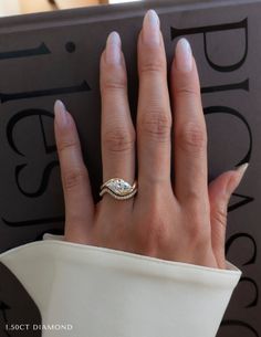 a woman's hand with a diamond ring on top of her finger next to a book