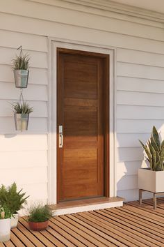 a wooden door on the side of a white house next to two potted plants