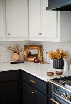 a white kitchen with black cabinets and gold accents on the counter top, along with an ornate framed photograph