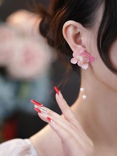 a woman with red nails and pink flowers on her ear