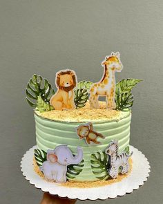 a hand holding a cake decorated with animals and plants