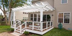 a deck with white railing and trellis on it in front of a house next to a tree