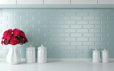 three white vases with red flowers in them on a countertop against a blue brick wall