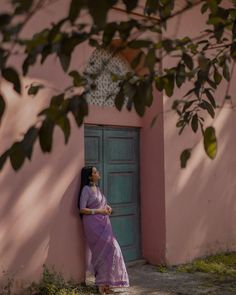 a woman in a purple dress leaning against a pink wall